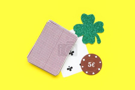 Poker chips, deck of cards and clover on yellow background. St. Patrick's Day celebration