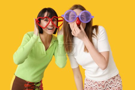 Foto de Hermosas mujeres jóvenes en gafas divertidas sobre fondo amarillo. Celebración del Día de los Inocentes - Imagen libre de derechos