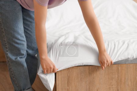 Mujer haciendo cama en dormitorio moderno, primer plano