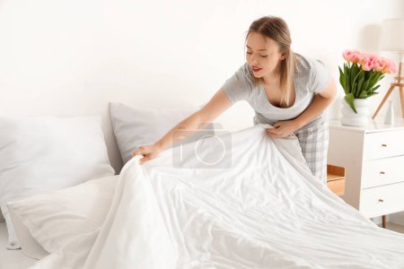 Photo for Pretty young woman making bed in modern bedroom - Royalty Free Image