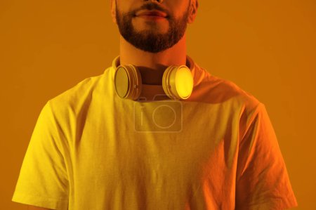 Young man in modern headphones on yellow background, closeup