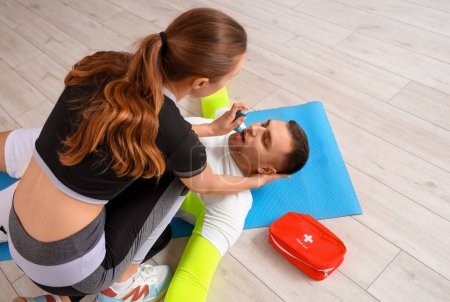 Female trainer with asthma inhaler giving man first aid in gym