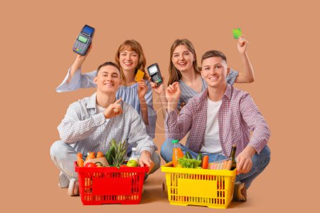 Young people with credit cards, payment terminals and shopping baskets on beige background