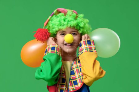 Foto de Muchacho divertido disfrazado de payaso con globos mostrando orejas sobre fondo verde. Celebración del Día de los Inocentes - Imagen libre de derechos