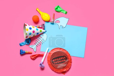Blank card with paper fishes, whoopee cushion and party decor on pink background. April Fools Day celebration