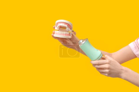 Weibliche Hände mit Mundspülmaschine und Kiefermodell auf gelbem Hintergrund
