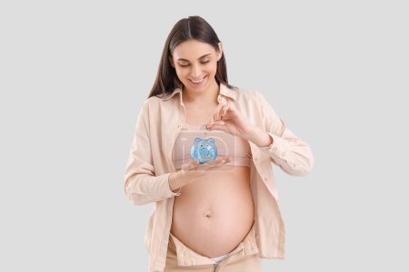 Young pregnant woman putting coin into piggy bank on light background. Maternity Benefit concept