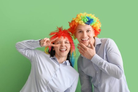 Foto de Compañeros de negocios con pelucas graciosas sobre fondo verde. Celebración del Día de los Inocentes - Imagen libre de derechos