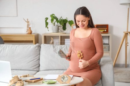 Young pregnant woman with baby rattle and money sitting at home. Maternity Benefit concept