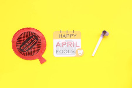 Festliche Postkarte zum Aprilscherz mit Trillerpfeife und Kissen auf gelbem Hintergrund
