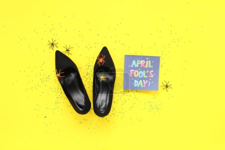 Shoes with fake spiders, sequins and festive postcard for April Fools Day on yellow background
