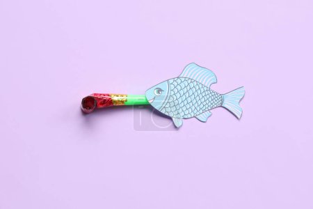 Foto de Papel de pescado con silbato de fiesta sobre fondo lila. Celebración del Día de los Inocentes - Imagen libre de derechos