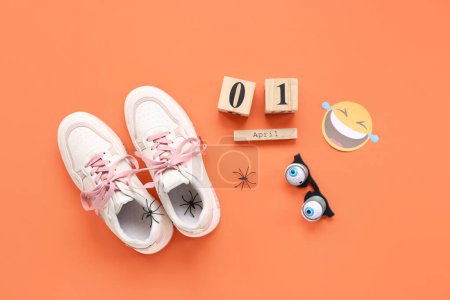 Shoes with tied together laces, fake spiders and calendar on orange background. April Fools Day celebration