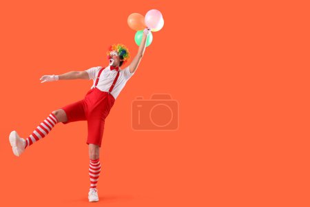 Portrait of surprised clown with balloons on orange background. April Fool's day celebration