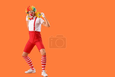 Foto de Retrato de payaso divertido con monopatín sobre fondo naranja. Celebración del día del tonto de abril - Imagen libre de derechos