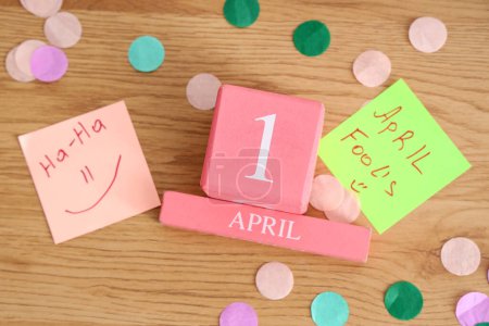 Foto de Calendario cubo con fecha 1 DE ABRIL, divertidas pegatinas de papel y confeti sobre fondo de madera. Celebración del Día de los Inocentes - Imagen libre de derechos