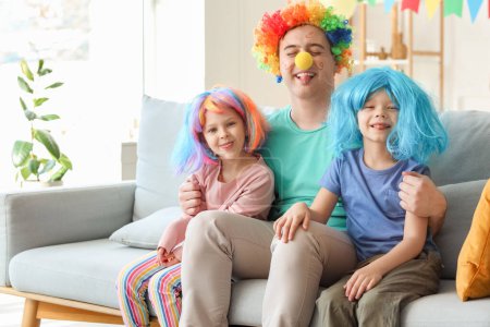 Foto de Padre y sus hijos con pelucas de colores en casa. Celebración del Día de los Inocentes - Imagen libre de derechos