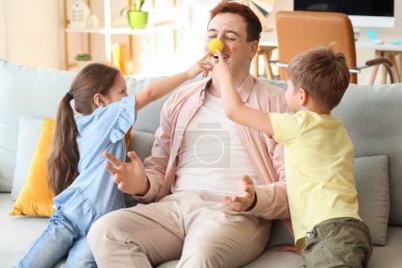 Niños pequeños bromeando a su padre con la nariz de payaso y pinturas de la cara en casa. Broma del Día de los Inocentes