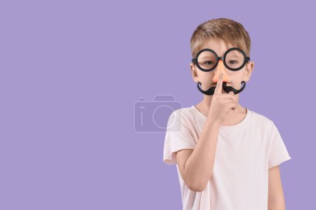 Foto de Lindo niño en disfraz divertido que muestra gesto de silencio sobre fondo lila. Celebración del Día de los Inocentes - Imagen libre de derechos