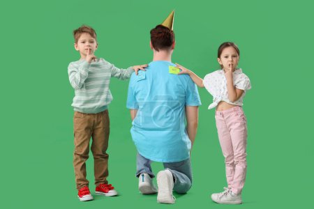 Kleine Kinder kleben Papieraufkleber auf den Rücken ihres Vaters auf grünem Hintergrund. Feier zum Aprilscherz