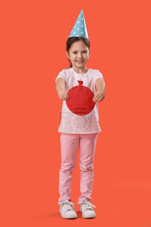Cute little girl with party hat and whoopee cushion on orange background. April Fool's Day celebration