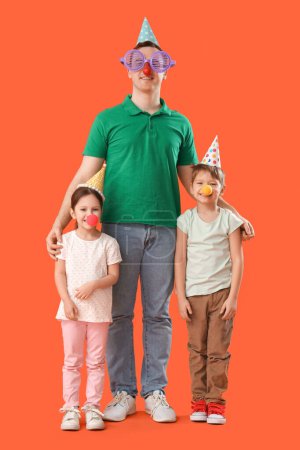 Foto de Padre y sus hijos pequeños con disfraces divertidos sobre fondo naranja. Celebración del Día de los Inocentes - Imagen libre de derechos