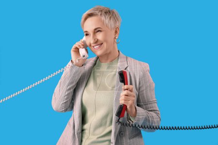 Mature woman with two telephone receivers on light blue background