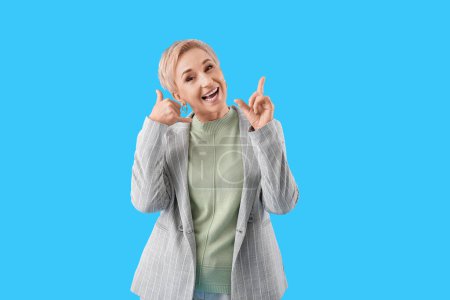 Cool mature woman showing "call me" gesture on light blue background
