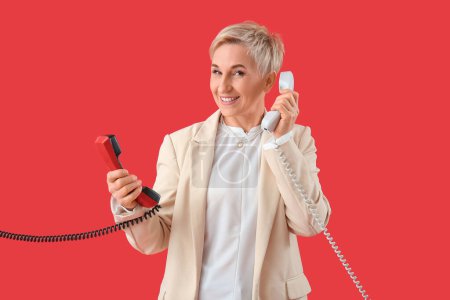 Mature woman with two telephone receivers on red background
