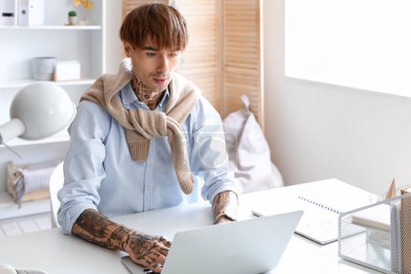 Schöne junge tätowierte Geschäftsmann arbeitet mit Laptop am Arbeitsplatz im Büro