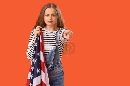 Junge Frau mit USA-Flagge zeigt auf Betrachter auf orangefarbenem Hintergrund. Anschuldigungskonzept