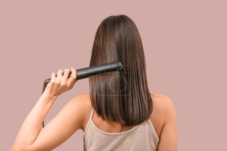 Photo for Beautiful young woman straightening hair on pink background, back view - Royalty Free Image
