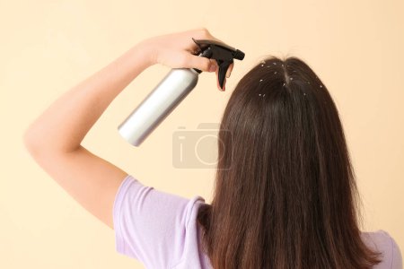 Junge Frau mit Schuppen-Problem beim Auftragen von Haarspray auf beigem Hintergrund, Rückseite