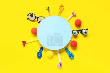 Blank card with funny glasses, clown noses and party decor on yellow background. April Fools Day celebration