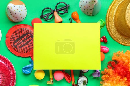 Blank card with whoopee cushion, funny glasses and party decor on green background. April Fools Day celebration