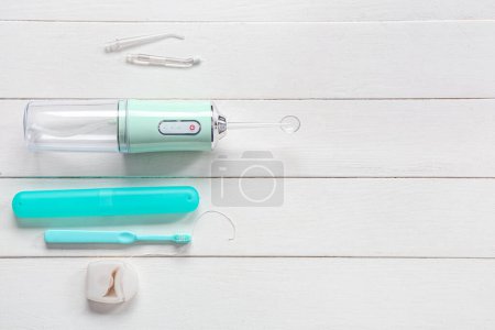 Téléchargez les photos : Arroseur buccal, brosse à dents, étui à brosse à dents et fil dentaire sur fond de bois blanc - en image libre de droit
