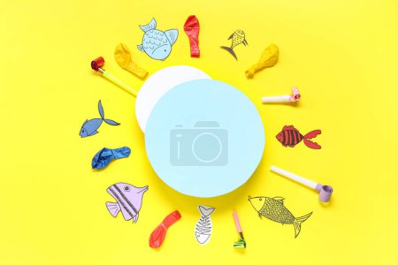 Foto de Tarjetas en blanco con peces de papel, globos y silbatos de fiesta sobre fondo amarillo. Celebración del Día de los Inocentes - Imagen libre de derechos