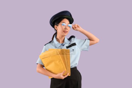 Young Asian postwoman with parcels on lilac background