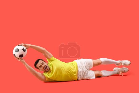Porträt eines männlichen Fußballspielers, der Ball auf rotem Hintergrund fängt