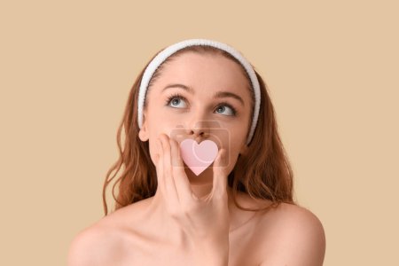 Beautiful young woman with heart-shaped sponge on beige background