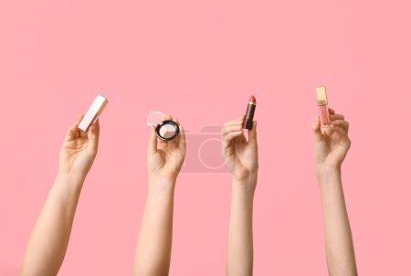 Foto de Manos femeninas con paleta de sombras de ojos, brillo de labios y lápiz labial sobre fondo rosa - Imagen libre de derechos