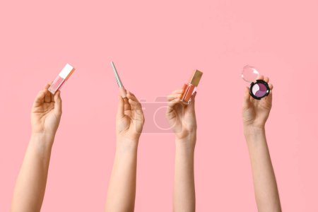 Foto de Manos femeninas con paleta de sombras de ojos, brillo de labios y delineador de ojos sobre fondo rosa - Imagen libre de derechos