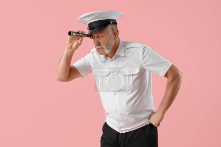 Photo for Mature sailor looking through spyglass on pink background - Royalty Free Image