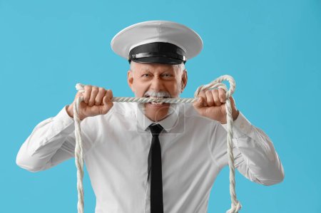 Mature sailor biting rope on blue background