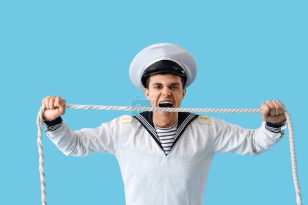 Angry young sailor with rope on blue background
