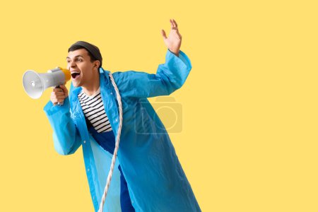 Photo for Young sailor in raincoat with rope shouting into megaphone on yellow background - Royalty Free Image
