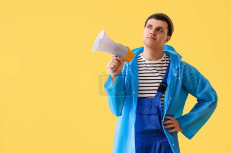 Thoughtful young sailor in raincoat with megaphone on yellow background