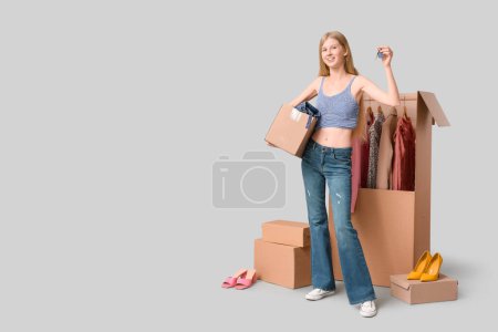 Foto de Hermosa mujer joven con llave de la casa y cajas de armario de ropa sobre fondo gris - Imagen libre de derechos