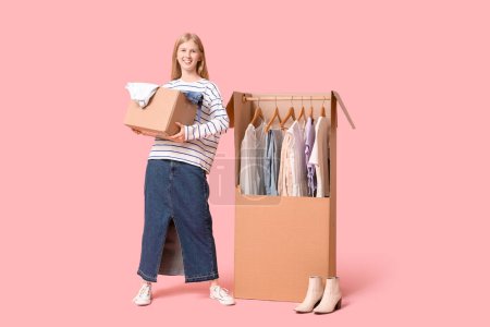 Foto de Hermosa joven feliz mujer y cajas de armario con ropa sobre fondo rosa - Imagen libre de derechos
