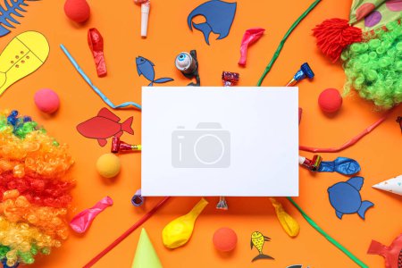 Blank card with paper fishes, clown wigs and party decor on orange background. April Fools Day celebration